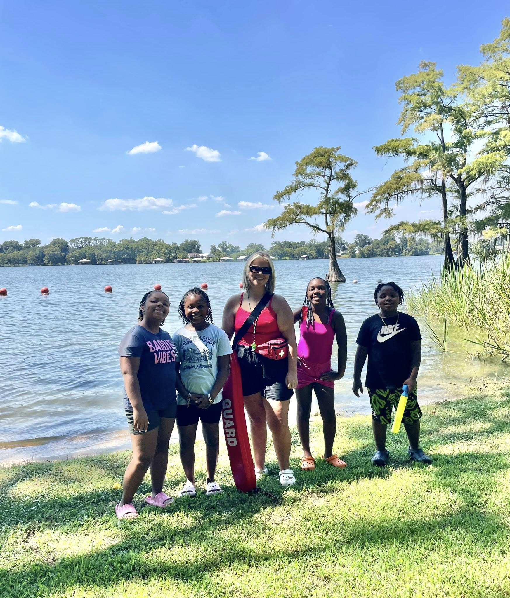 A woman and four kids standing by a lake.